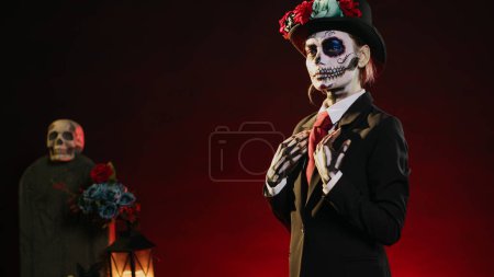 Photo for Smiling horror woman wearing santa muerte costume in studio, having black and white skull make up. Celebrating day of the dead holy mexican tradition, festival body art horror look. Handheld shot. - Royalty Free Image