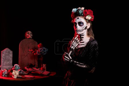 Photo for Beautiful woman wearing traditional skull body art and santa muerte costume in studio, acting like holy goddess of death to celebrate day of the dead. Mexican traditional holiday with make up. - Royalty Free Image