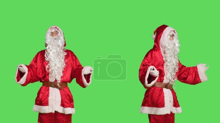 Photo for Santa claus festive embodiment on december celebration posing over greenscreen backdrop. Confident young man in seasonal winter costume with glasses and beard, spreading happiness. - Royalty Free Image