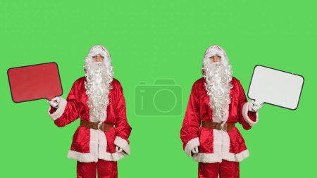 Foto de Papá Noel usando la burbuja del habla en la cámara, haciendo publicidad de invierno estacional con una persona vestida como Papá Noel. Hombre alegre en traje rojo sosteniendo billar con copyspace. - Imagen libre de derechos