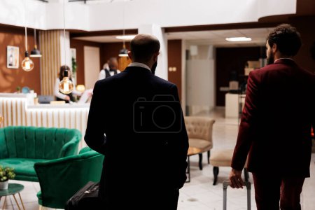 Photo for Business travellers arriving at hotel, approaching front desk to register. Two partners in formalwear travelling to meet with CEO and discuss about new project, receive excellent concierge services. - Royalty Free Image