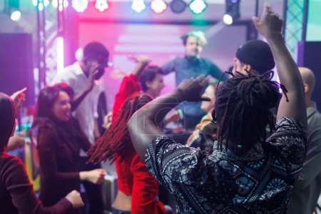 Diverse people dancing and raising hands at discotheque with live music in nightclub. Young clubbers partying, moving to electronic music rhythm and jumping on club dancefloor