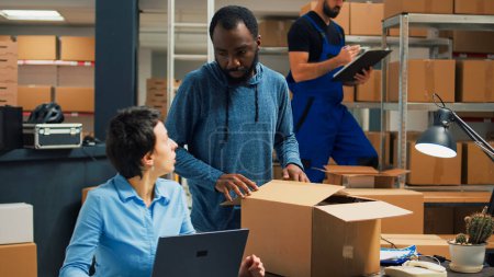 Téléchargez les photos : Small business owners doing quality control before shipping products order, packing merchandise in cardboard boxes. Workers preparing delivery and shipment in warehouse storage room. - en image libre de droit