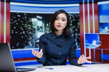 Photo for Talk show host presenting daily news and latest events on live television channel to cover worldwide topics, tv reportage. Asian woman discussing celebrity scandals in newsroom studio. - Royalty Free Image