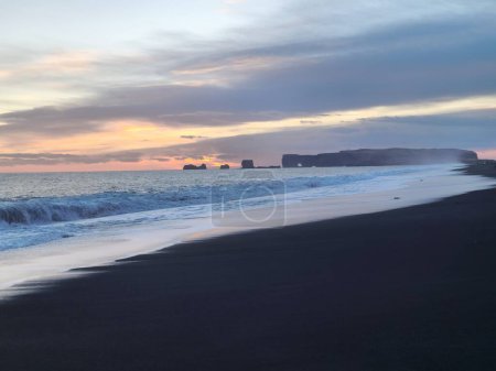Foto de Playa islandesa de arena negra en el norte, hermosa costa del océano y frente al mar al atardecer majestuoso paisaje icelandés. Increíble costa atlántica con enormes olas persiguiendo en tierra. - Imagen libre de derechos