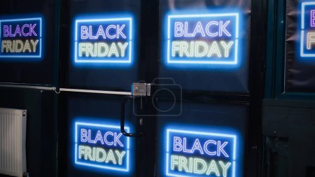 Téléchargez les photos : Store entrance decorated on black friday with neon signs, inside shopping center. Clothing shop interior with fashion items on racks, waiting for customers to buy products on shopping day. - en image libre de droit