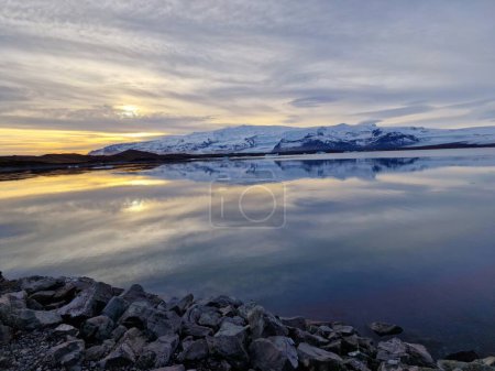 Téléchargez les photos : Lac glacial avec des collines enneigées au loin, ciel coloré heure dorée en iceland. avec de l'eau glacée. Belle nature sauvage dans la région du nord paysage et nature glaciaire. - en image libre de droit