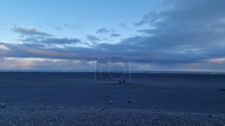 Téléchargez les photos : Cadre islandais en bord de mer au coucher du soleil avec ciel rose et pâturages gelés, plage de sable noir offrant une vue pittoresque. Paysages autour d'immenses eaux libres dans un environnement glaciaire. - en image libre de droit