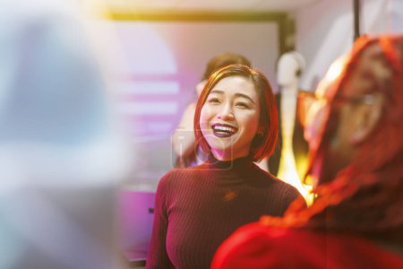 Téléchargez les photos : Sourire femme asiatique heureuse faire la fête dans une boîte de nuit avec des projecteurs et avoir du plaisir. Fille gaie dansant et clubbing à la discothèque, profiter du divertissement de la vie nocturne dans le club - en image libre de droit
