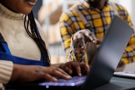 Photo for African american woman warehouse worker hands typing on laptop. Storehouse employee checking stock supply schedule online, using goods inventory management computer software close up - Royalty Free Image