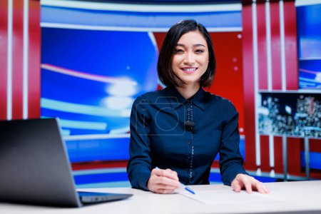 Photo for Asian presenter on daily newscast in newsroom, talking about latest international events on live broadcast. Woman reporter creating television content with media outlets headlines. - Royalty Free Image