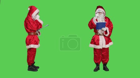 Photo for Saint nick writing data on clipboard, creating naughty or nice list of children before sending gifts for christmas eve celebration. December main character take notes on files, greenscreen. - Royalty Free Image