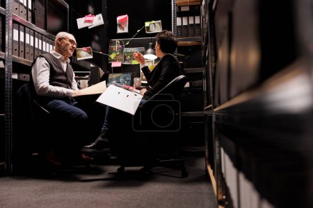 Photo for Investigators working overtime at criminal investigations in arhive room, analyzing missing person case. Private detectives checking crime scene evidence, discussing mysterious suspect report - Royalty Free Image