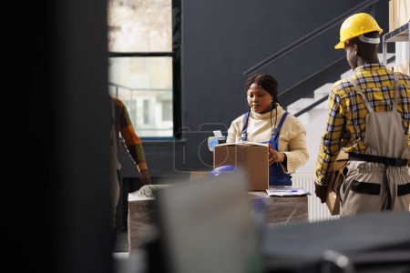 Téléchargez les photos : Femme afro-américaine employée de bureau de poste scellant le colis et préparant la commande du client pour le transport. Entreprise d'expédition employé fermeture boîte en carton avec ruban adhésif dans l'entrepôt - en image libre de droit