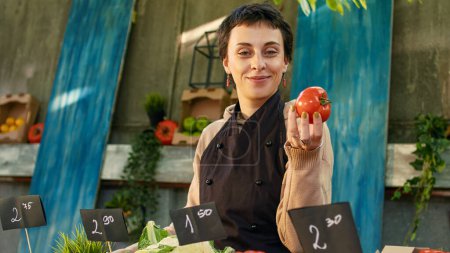 Photo for Young greengrocer with apron showing organic farming produce, arranging colorful bio fruits and veggies on stand. Small business farmers market owner selling natural fresh products. - Royalty Free Image