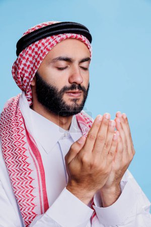 Téléchargez les photos : Homme musulman religieux les yeux fermés priant Dieu à bras ouverts. Arabe habillé en ghutra coiffure et robe vêtements traditionnels dans la pose de prière montrant culte et concept de foi - en image libre de droit