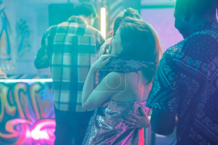 Photo for Women hugging in nightclub while attending discotheque party. Girlfriends embracing on dancefloor with spotlights while dancing and enjoying nightlife entertainment in club at night - Royalty Free Image