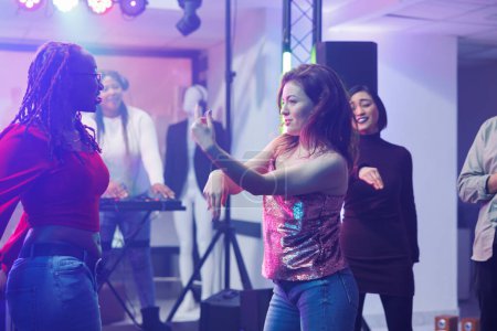 Photo for Energetic women dancers improvising moves while clubbing and enjoying nightlife leisure activity. Girlfriends doing dance battle on dancefloor at discotheque party in nightclub - Royalty Free Image