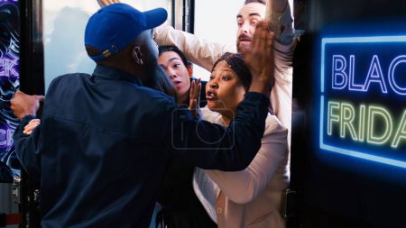 Téléchargez les photos : Divers acheteurs se disputent avec le gardien de sécurité, attendant les offres du vendredi noir à l'extérieur du grand magasin. Clients anxieux fous impatients devant l'entrée du centre commercial. - en image libre de droit