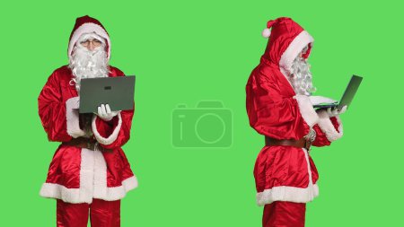 Photo for Saint nick using laptop on videocall, talking to people on online videoconference meeting and browsing online page. Modern person holding pc wireless on chat on teleconference, greenscreen. - Royalty Free Image