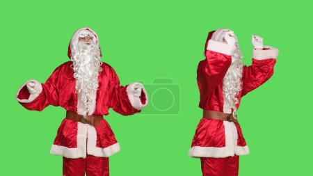 Photo for Santa choirmaster conducting orchestra, musical chief accompany music notes in studio over greenscreen. Father christmas acting like musical conductor, musician singing on camera. - Royalty Free Image