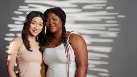 Téléchargez les photos : Happy diverse ladies hugging and posing in studio, promoting wellness and bodycare, self acceptance. Flawless young women with different body shapes and skintones showing self love. - en image libre de droit