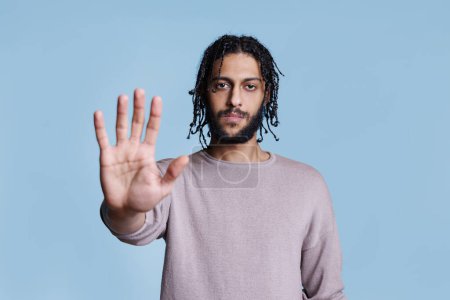 Téléchargez les photos : Un homme arabe faisant un geste d'arrêt à la main et regardant la caméra avec un portrait sérieux de l'expression du visage. Jeune confiant montrant un signe d'avertissement et de rejet avec concept de bras - en image libre de droit
