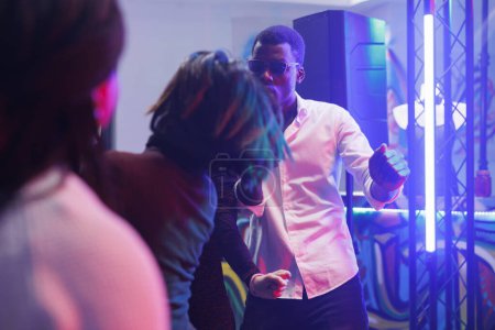 Cool african american man partying and dancing in nightclub illuminated with vibrant lights. Clubbers having fun on dancefloor in crowded club while attending discotheque
