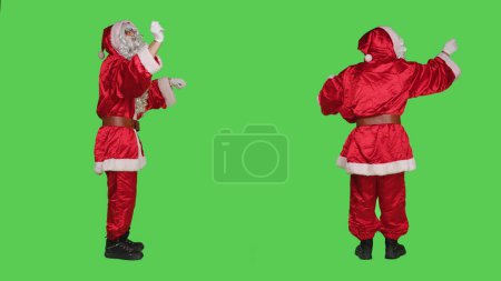 Photo for Saint nick musician accompany orchestra to sing, choir master conducting music notes on camera over greenscreen backdrop. Father christmas performing as musical director, christmas eve. - Royalty Free Image