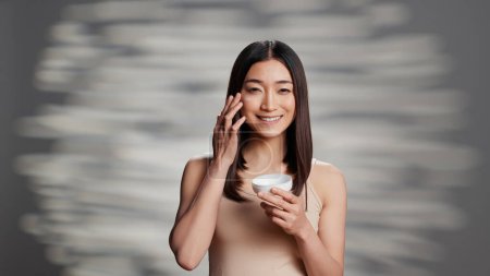 Photo for Young radiant person applying moisturizing cream to promote skincare routine and uplifting products. Beauty model using face serum and moisturizer for new cosmetology ad campaign. - Royalty Free Image