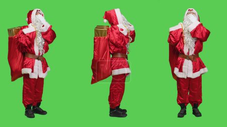 Photo for Sleepy person in santa suit yawning against full body greenscreen, feeling exhausted of carrying bag with presents and toys for december holiday. Saint nick embodiment feeling tired. - Royalty Free Image