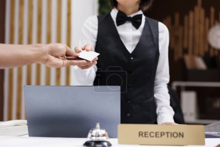 Photo for Front desk staff giving key card to man, helping to gain access to hotel room with cardkey reader. Tourist filling in registration forms and doing check in at reception counter. Close up. - Royalty Free Image
