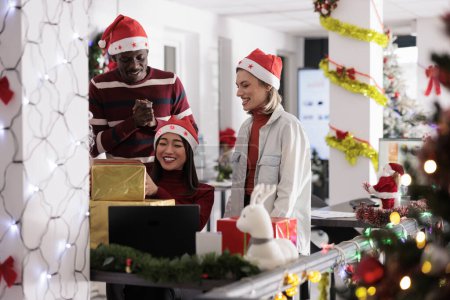 Téléchargez les photos : Des employés heureux qui applaudissent après avoir reçu des cadeaux du Père Noël pendant la fête de Noël. Travailleurs joyeux appréciant les cadeaux dans un espace de travail décoré pendant la saison des vacances d'hiver - en image libre de droit