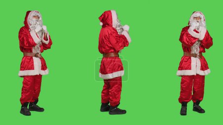 Photo for Saint nick hail someone on camera, asking people to come over and join him. Father christmas embodiment in costume calling person to accompany, full body greenscreen background. - Royalty Free Image