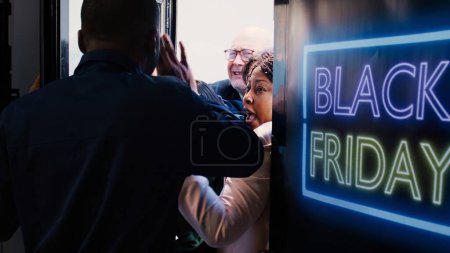 Photo for Customers shoving each other out of way to enter store first during black friday shopping spree. African american security agent holding back crazy shoppers breaking inside shopping center. - Royalty Free Image