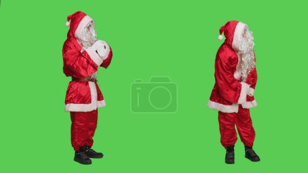 Foto de Santa cosplay comprobar el tiempo en reloj de pulsera, de pie sobre la pantalla verde de cuerpo completo en el estudio. Papá Noel vistiendo traje rojo famoso con barba blanca, actuando impaciente en la cámara. - Imagen libre de derechos
