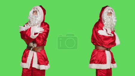 Foto de Santa Claus carácter celebración de invierno sobre fondo de pantalla verde, persona segura positiva en traje festivo tradicional con sombrero y barba. Joven difundiendo espíritu navideño. - Imagen libre de derechos