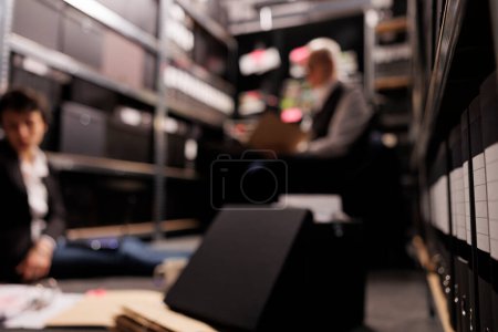 Photo for Selectiv focus of storage full with investigation evidence files, in background criminology team analyzing crime scene report. Private detectives working overtime at federal case in arhive room - Royalty Free Image