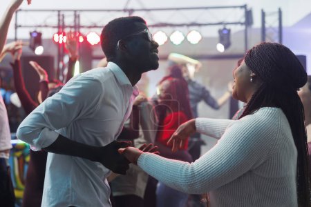 Téléchargez les photos : Couple afro-américain insouciant dansant ensemble et s'amusant dans une boîte de nuit. Joyeux jeune homme et femme clubbers tenant la main et faisant la fête sur la piste de danse tout en clubbing - en image libre de droit