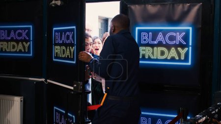 Photo for Crowd of diverse clients at entrance pushing to open front door, going crazy on black friday. People customers arguing with african american security agent waiting in line. Bargain hunting. - Royalty Free Image