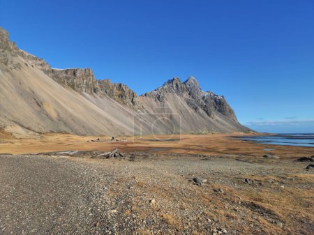 Téléchargez les photos : Célèbres montagnes de vestrahorn sur la plage avec d'énormes collines rocheuses dans un paysage nordique incroyable et des champs en Islande. Plage Stokksnes créant un cadre naturel hivernal, littoral de l'océan Arctique. - en image libre de droit