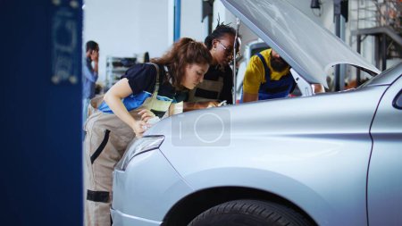 Photo for Team of mechanics in car service using inspection lamp to fix automobile in need of repairments. Colleagues service broken vehicle, checking for faulty engine using professional tools, dolly out shot - Royalty Free Image