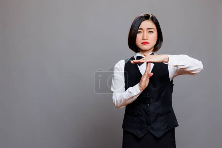 Photo for Confident asian waitress wearing uniform showing timeout sign with arms portrait. Restaurant serious woman employee asking to take break while making gesture with hands and looking at camera - Royalty Free Image
