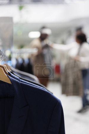 Photo for Trendy shirts hanging on rack in shopping mall with couple choosing clothes on blurred background. Casual menswear apparel on hangers in fashion boutique close up selective focus - Royalty Free Image