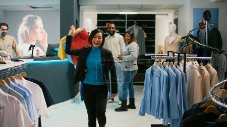 Photo for Asian customer doing dance moves with shopping bags, feeling happy after making purchase at cash register. Young woman dancing and buying trendy clothes at shopping mall. Tripod shot. - Royalty Free Image