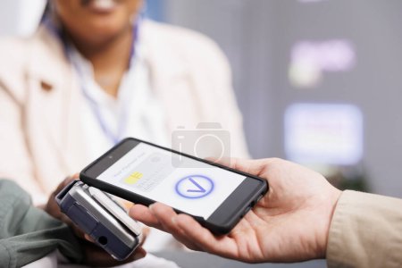 Photo for Close up of male customer holding smartphone making nfc contactless payment with electronic credit card, paying for clothes at cashier desk, selective focus. Shopper using mobile payment app - Royalty Free Image