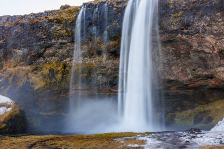 Photo for Arctic landscape of icelandic waterfall running down cliff, seljalandsfoss cascade with river flow falling off of hills in scandinavian polar scenery. Large water stream in wilderness. - Royalty Free Image