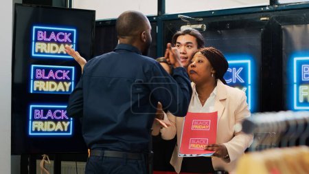 Photo for Angry clients pushing security guard, forcing to break red tape and buy clothes on promotional prices. Black friday anxious behaviour, crowd of diverse people in line at clothing store. Handheld shot. - Royalty Free Image