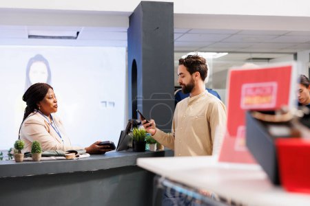 Photo for Male customer holding smartphone making contactless payment while shopping for clothes in fashion boutique. Young man standing at clothing store cashier counter using mobile phone to pay for purchases - Royalty Free Image