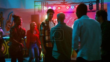 Photo for Happy adults improvise breakdance battle at club party, jumping around on dance floor with disco music and spotlights. Group of people showing off cool moves at nightclub. Handheld shot. - Royalty Free Image